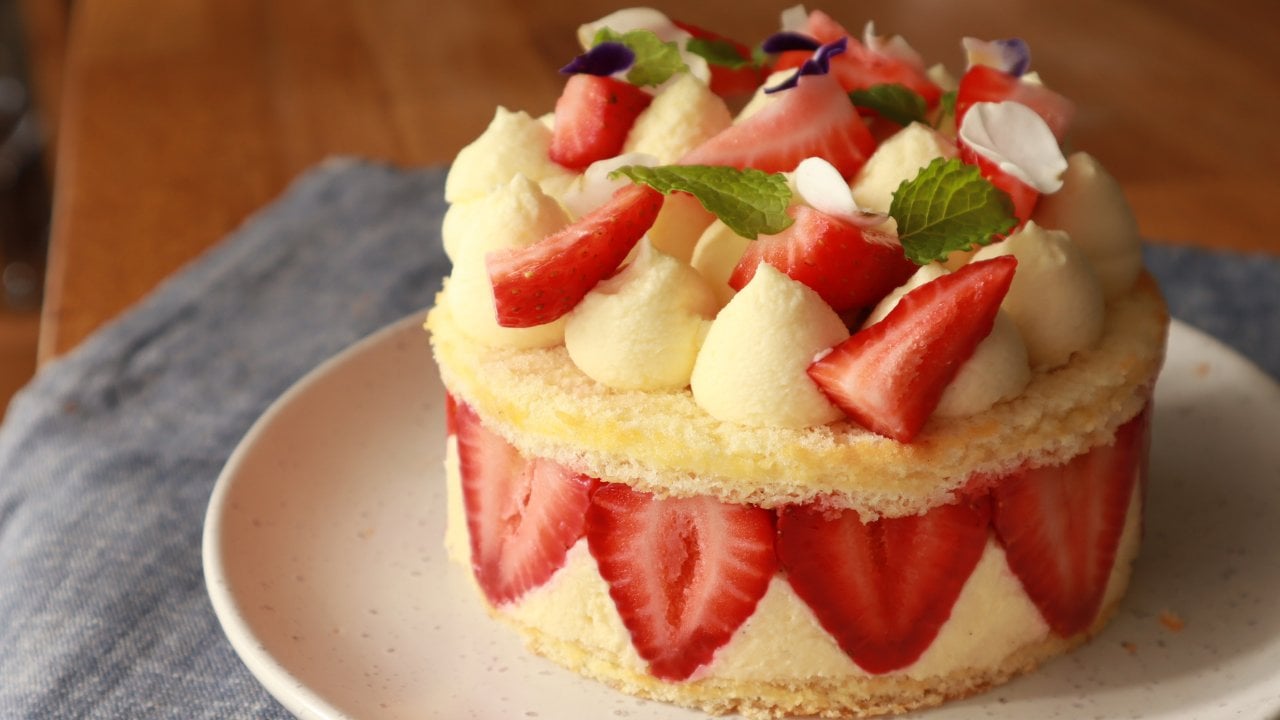 Chef de pastelaria feminino mantém um bolo decorado com flores sobre fundo  branco