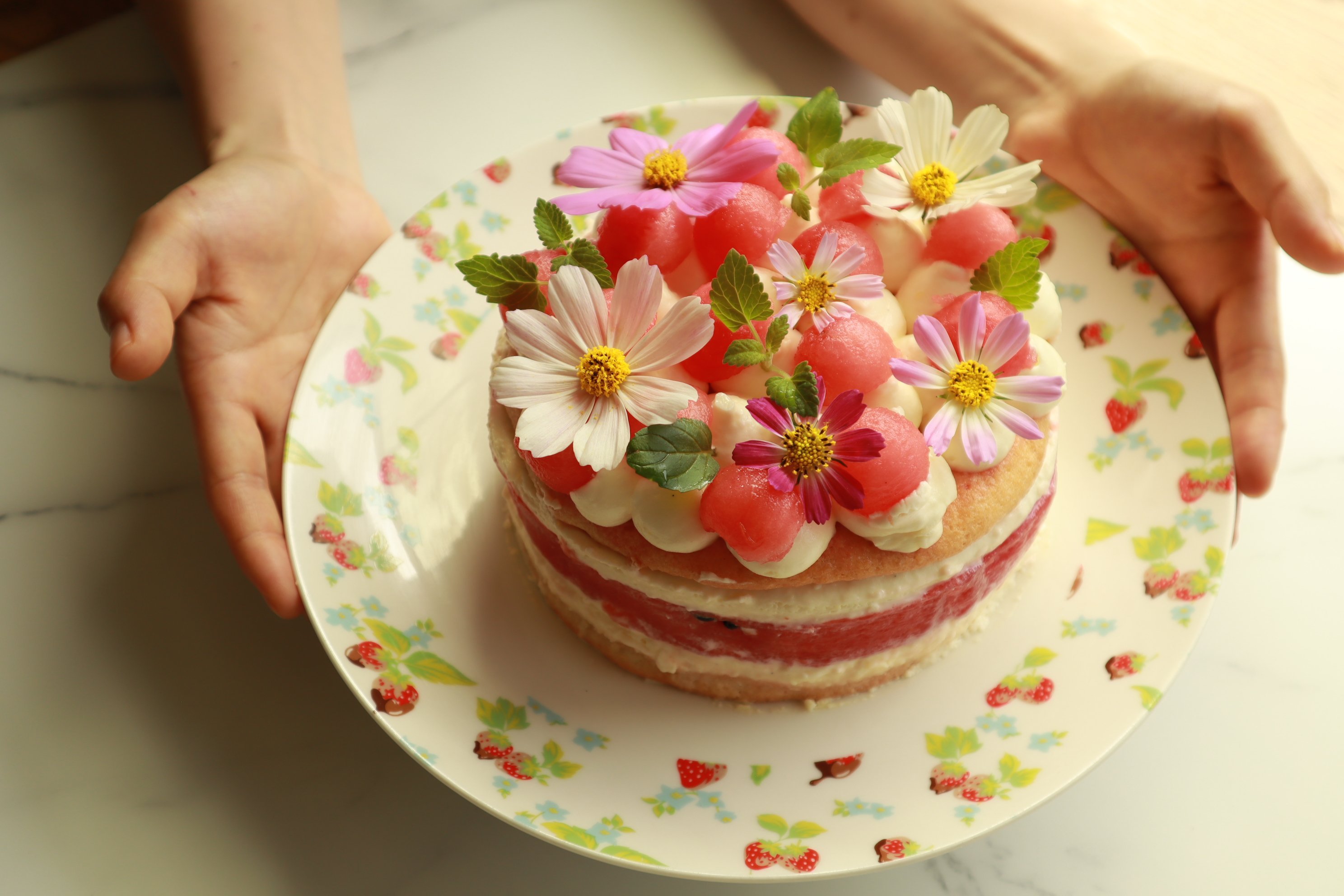 Chef de pastelaria feminino mantém um bolo decorado com flores sobre fundo  branco